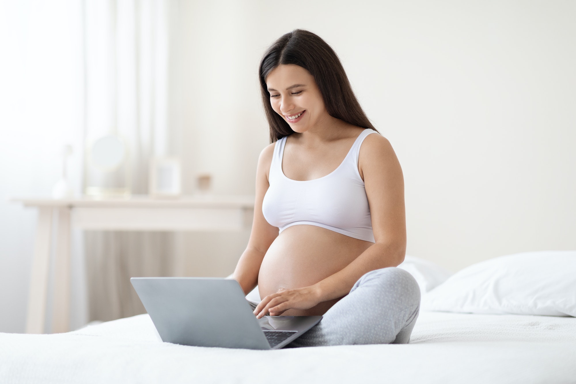 Happy pregnant woman using computer at home for laser depilation