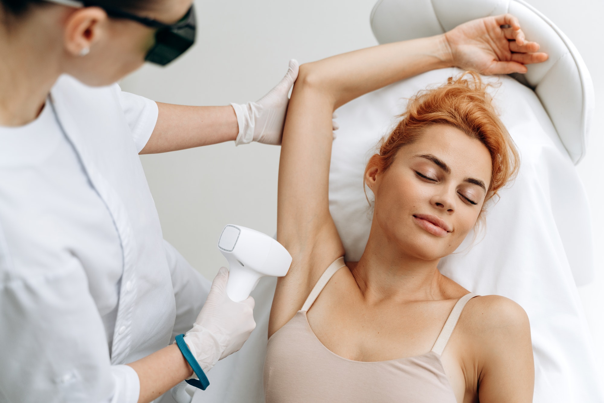 Portrait of young relaxed woman in underwear having professional laser epilation procedure of armpit