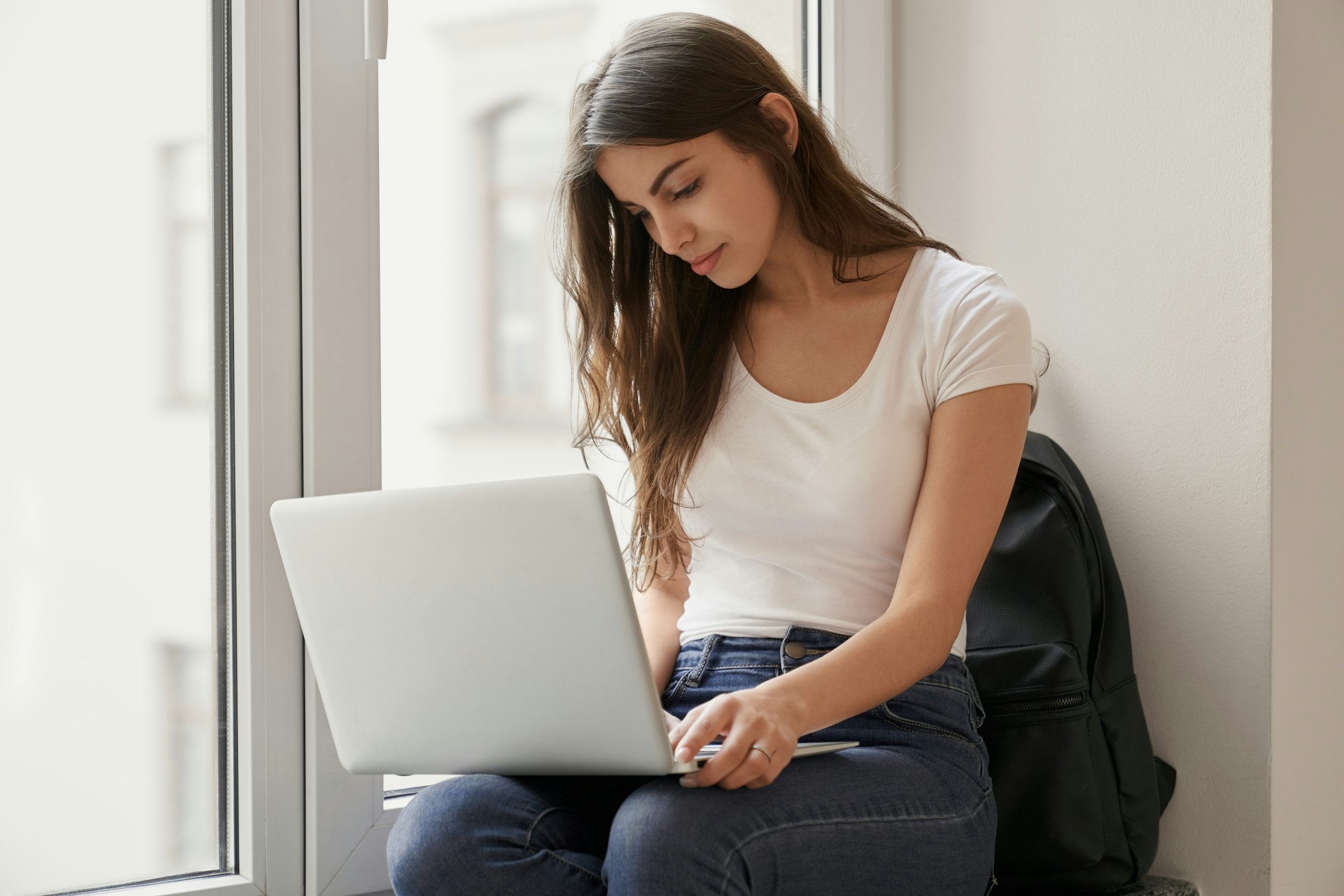 Pretty girl sitting on windowsill with laptop in university looking for advices for hyaluronic acid injections