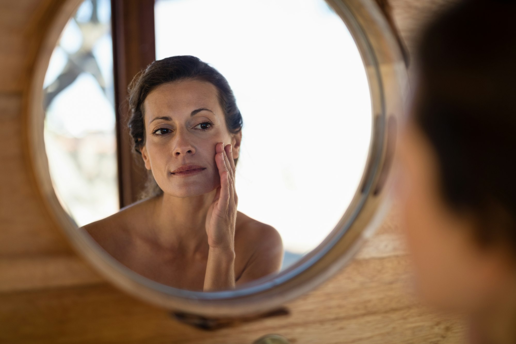 Woman looking at mirror worrying after oedema after hyaluronic acid injection