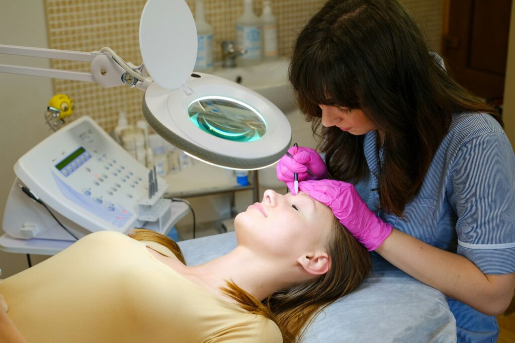 Young woman dermatologist doing hair removal treatment on patient's face with electrolysis