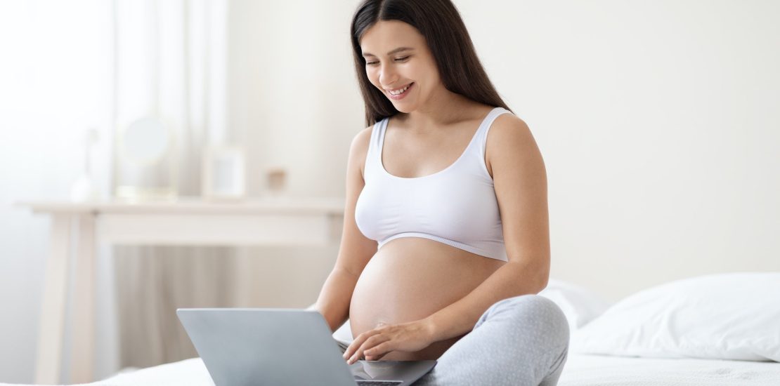 Happy pregnant woman using computer at home for laser depilation